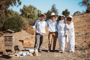 Four people in bee suites with a beehive