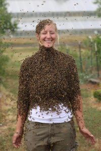 Smiling woman covered in honey bees.